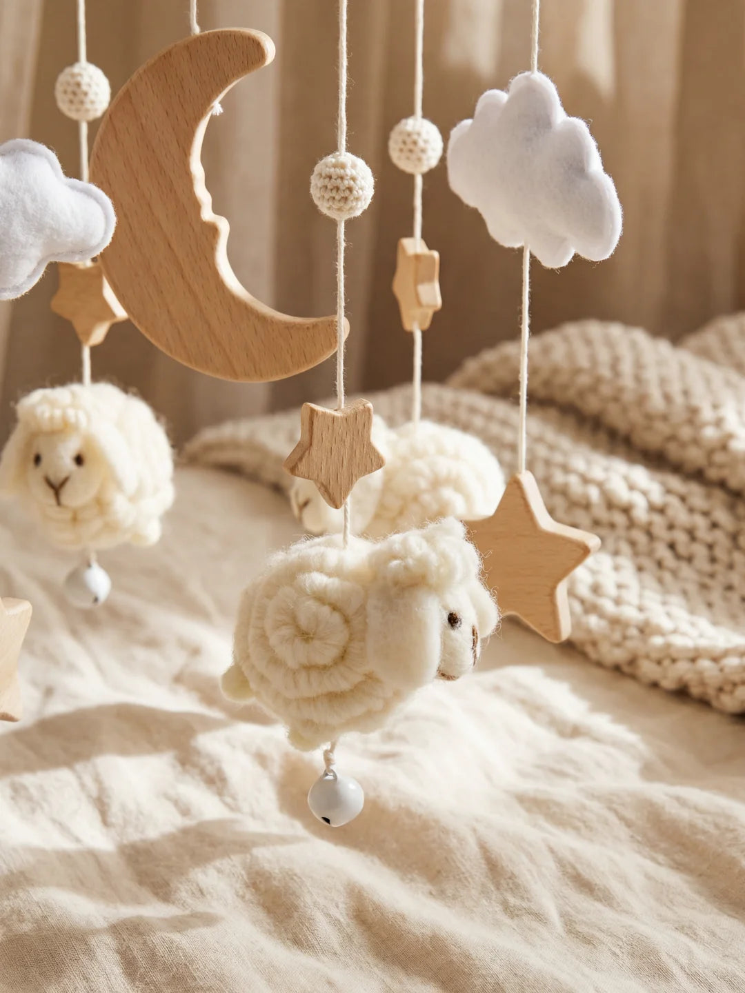 Détail d'un mouton en laine crème et de pompons crochetés sur un mobile bébé artisanal.