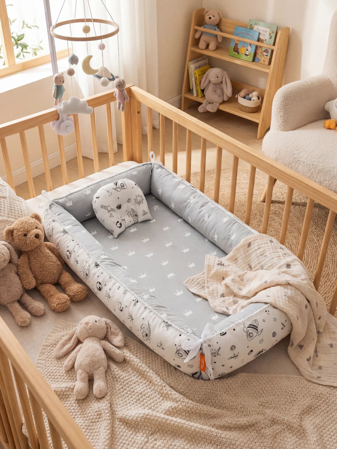 Réducteur de lit bébé gris avec motifs couronnes et illustrations d'espace (fusées, planètes) dans une chambre d'enfant.