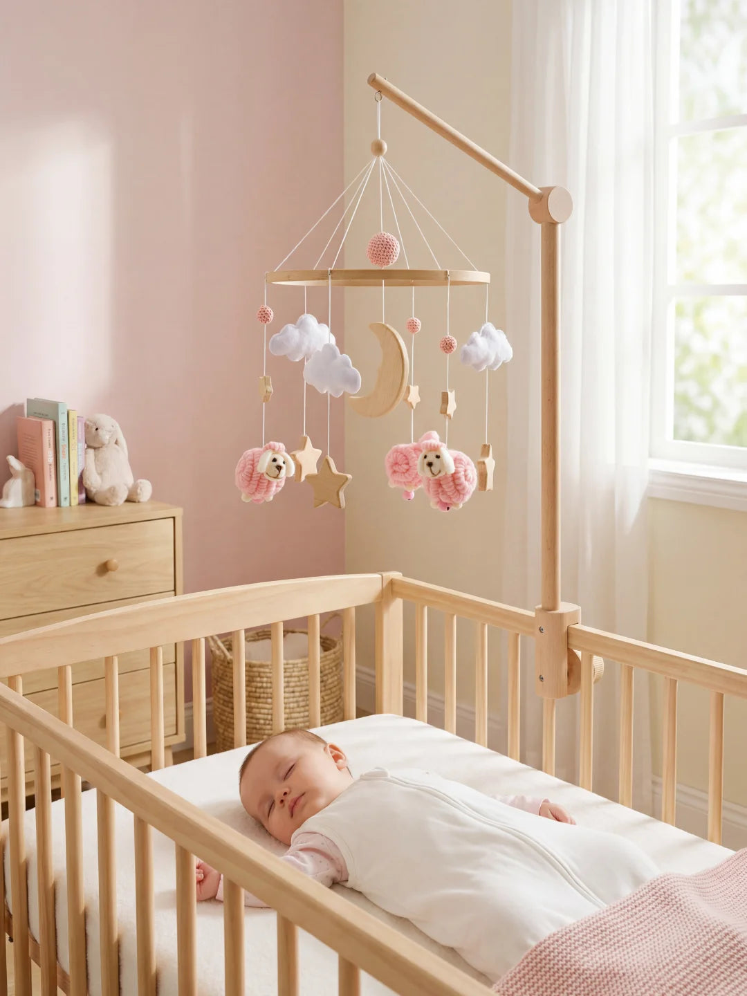 Bébé endormi dans son berceau sous un mobile de moutons roses dans une chambre aux tons pastel.