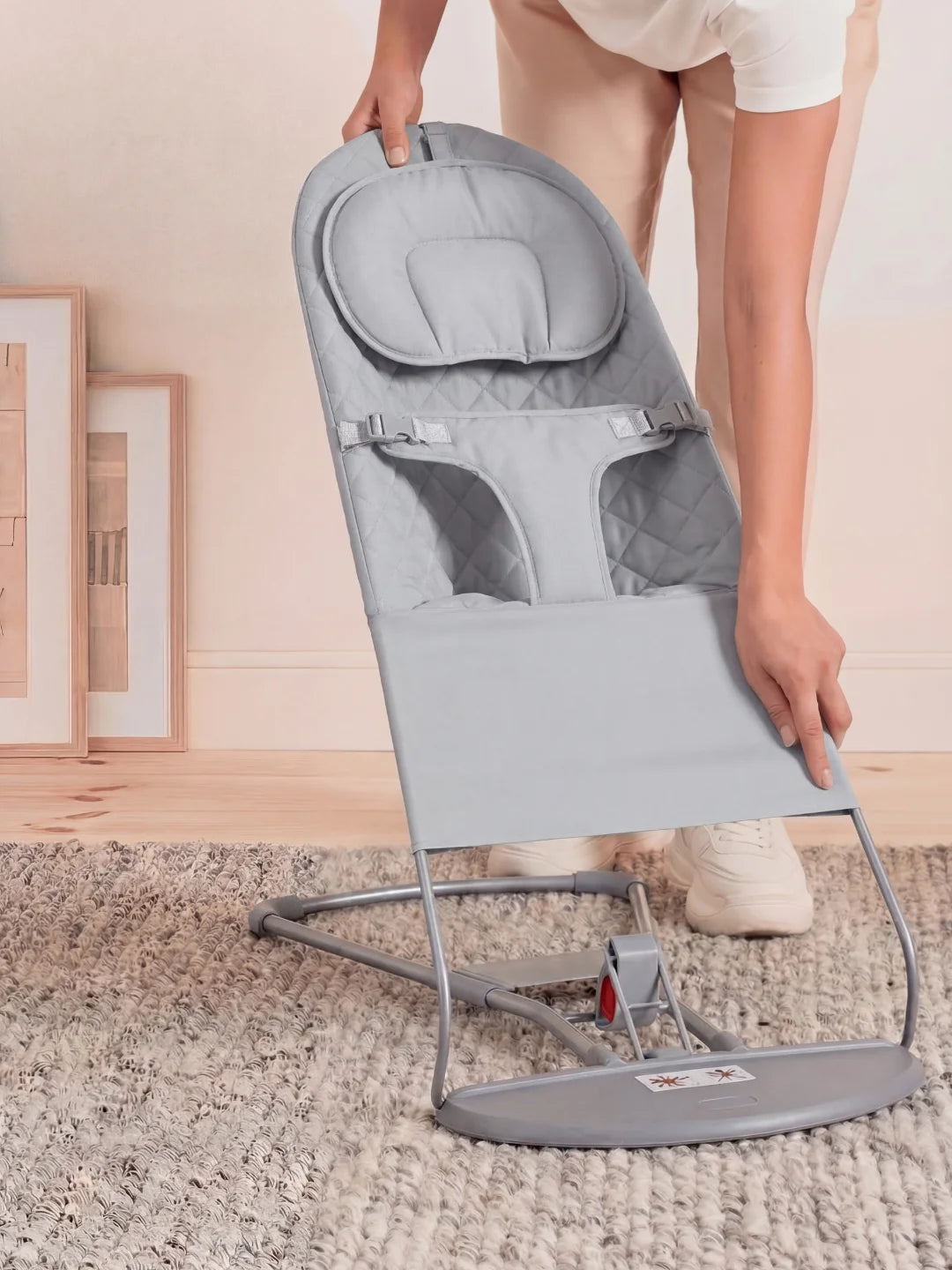 Mains d'un parent ajustant l'assise d'un transat pour bébé gris chiné sur un tapis épais.