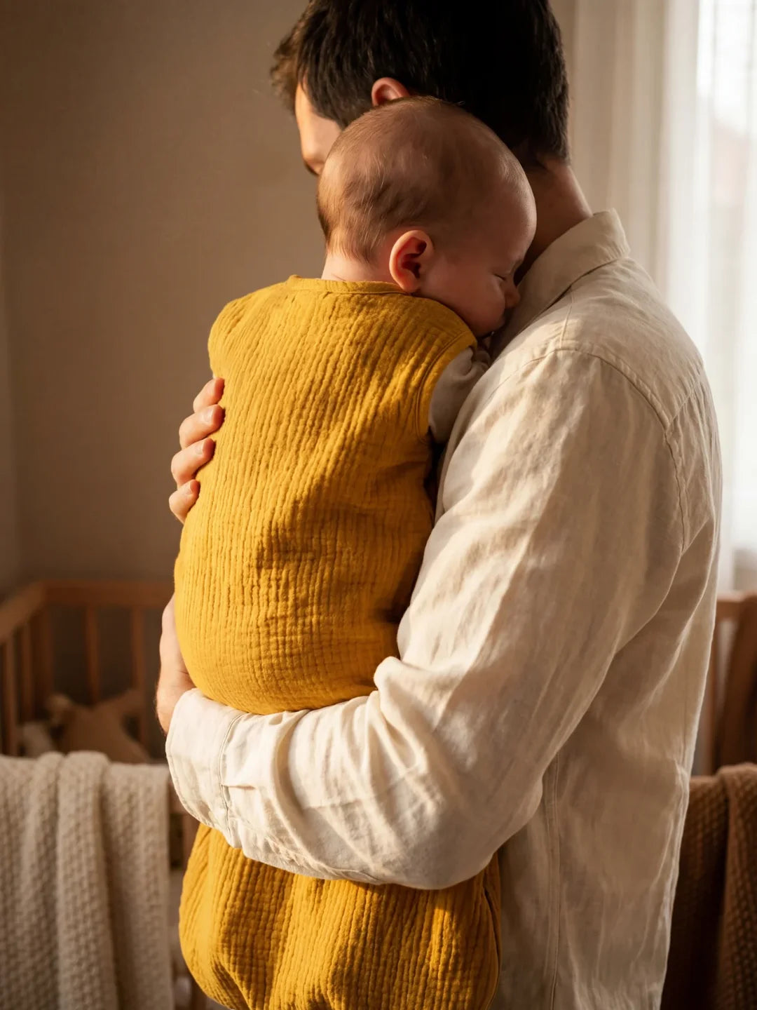 Maman portant bébé endormi dans sa gigoteuse gaze de coton moutarde près fenêtre