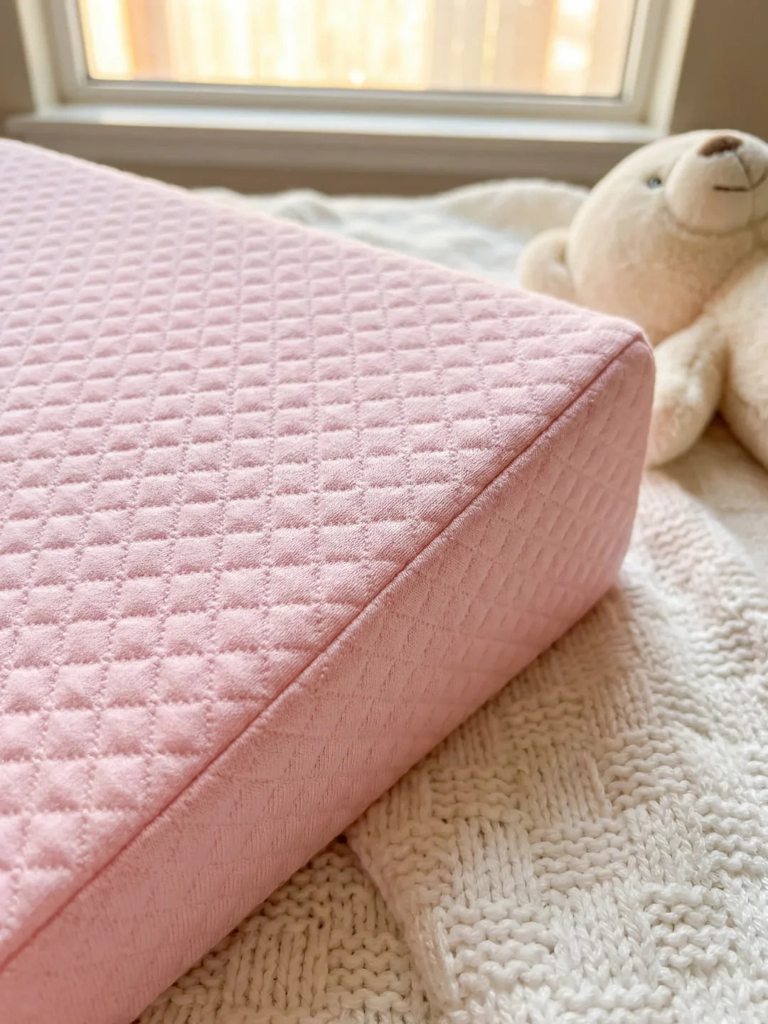 plan incliné rose matelassé pour bébé posé dans un lit à barreaux