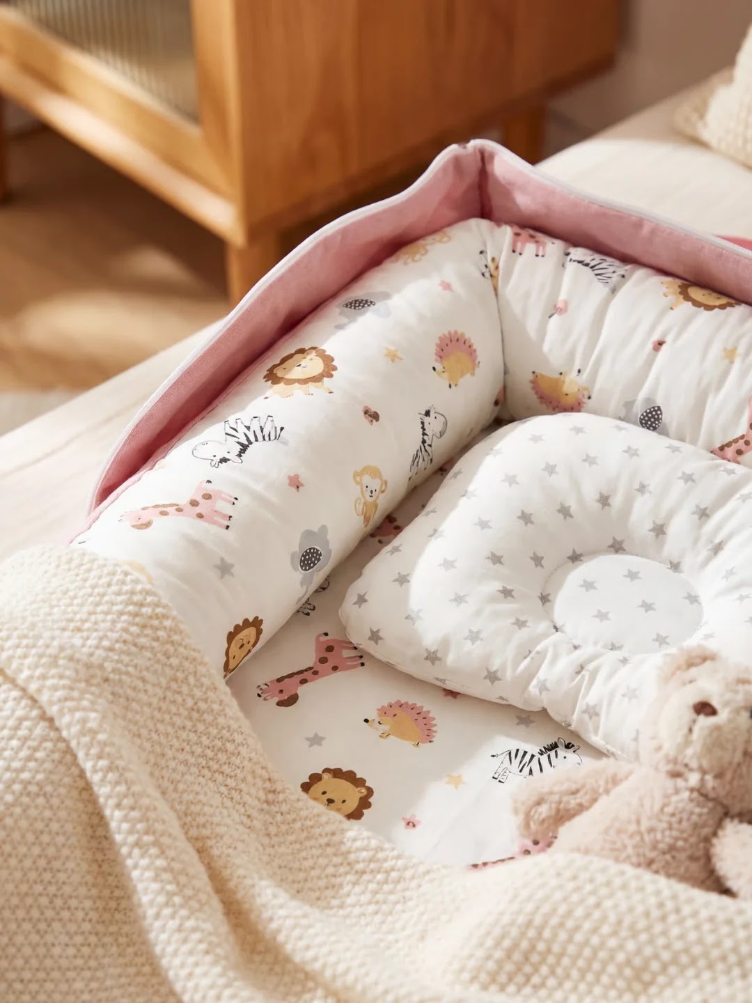 Réducteur de lit pour bébé avec motifs d'animaux, couleur rose et beige, vue de face avec couverture et peluche.