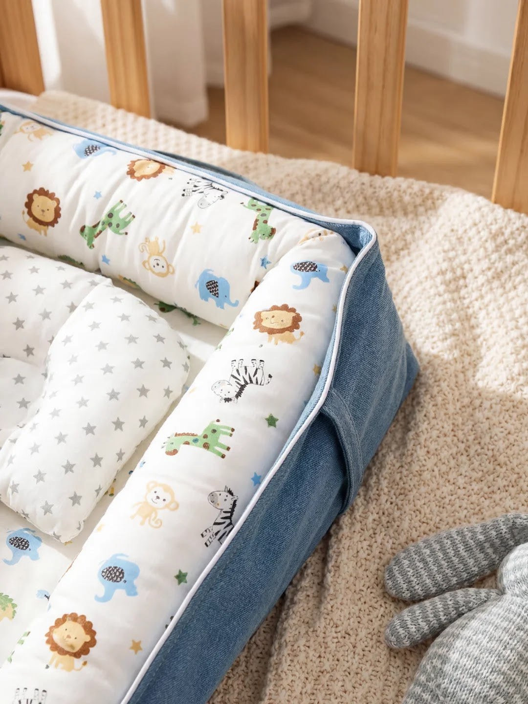 Réducteur de lit bébé avec motifs animaux et bordure bleue en profil, posé sur une couverture beige.