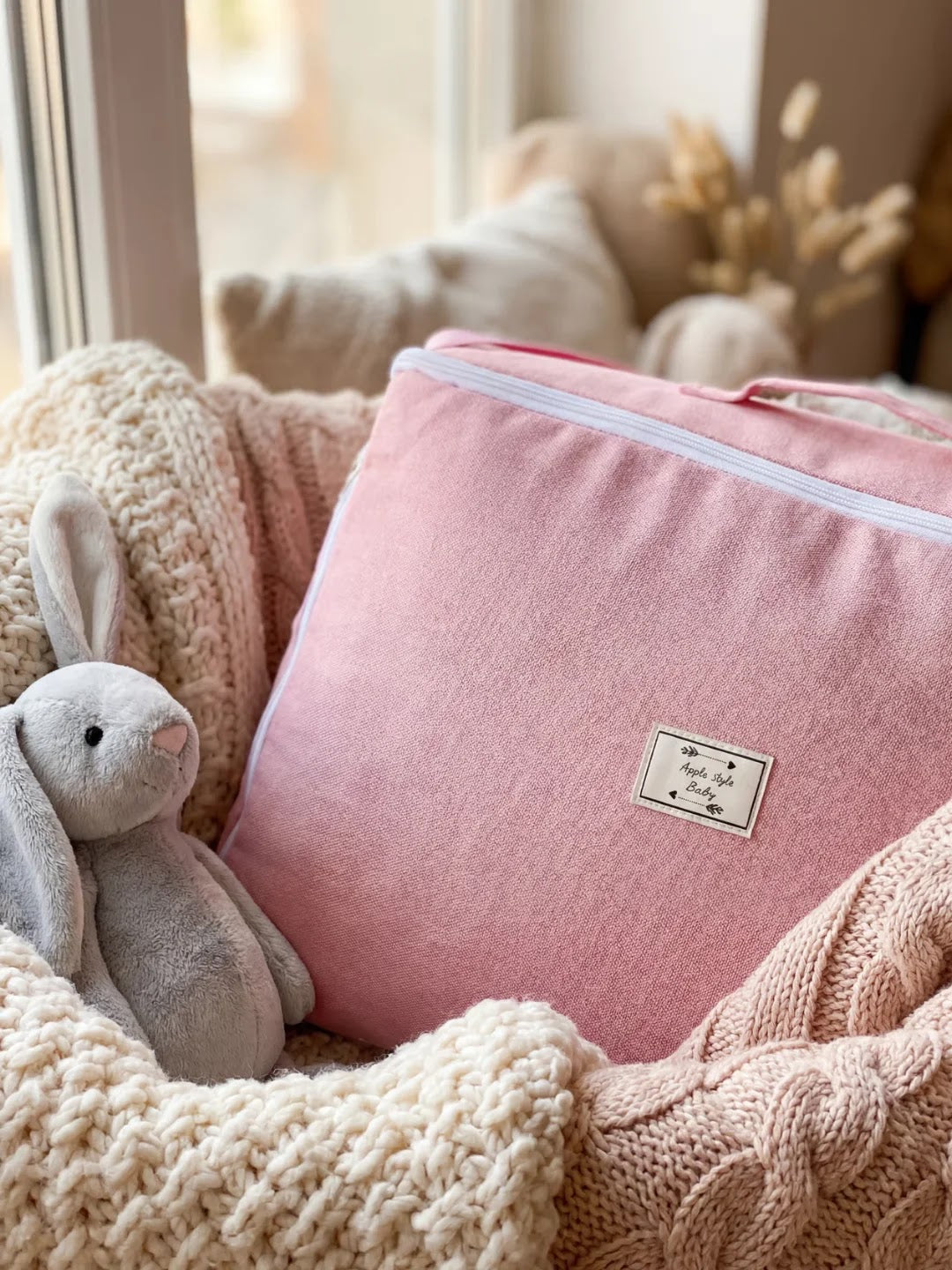 Réducteur de lit rose plié avec peluche lapin gris sur couverture tricotée.