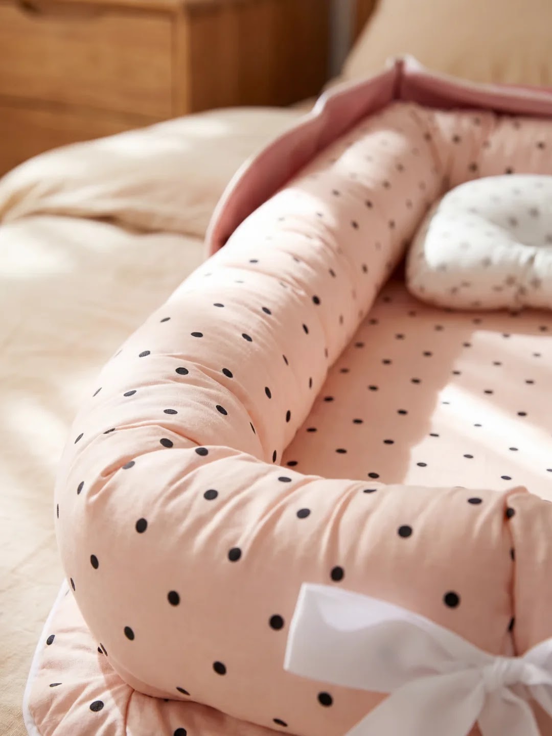 Réducteur de lit rose à pois noirs sur un lit beige avec coussin assorti.