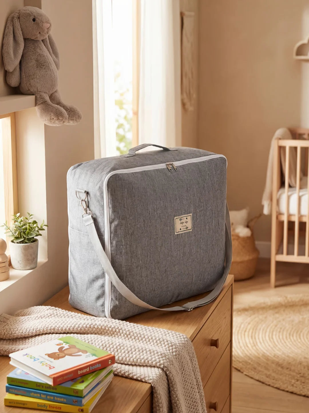 Sac de transport gris avec bandoulière pour réducteur de lit bébé posé sur une commode de nursery