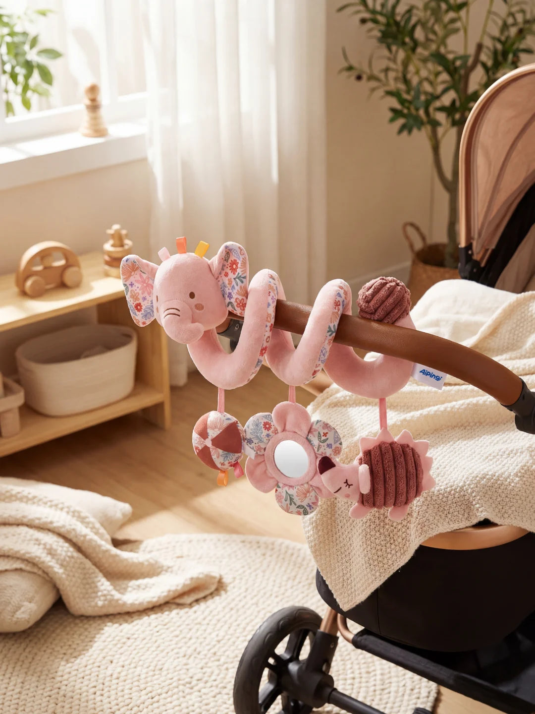 Spirale d'éveil éléphant rose avec motifs fleuris installée sur la barre d'une poussette.