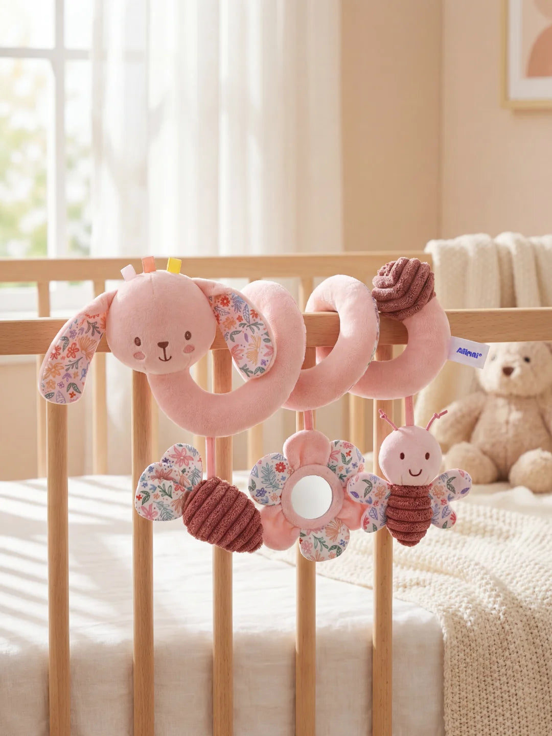 Spirale d'éveil lapin rose avec grandes oreilles fleuries fixée sur un lit de bébé blanc.