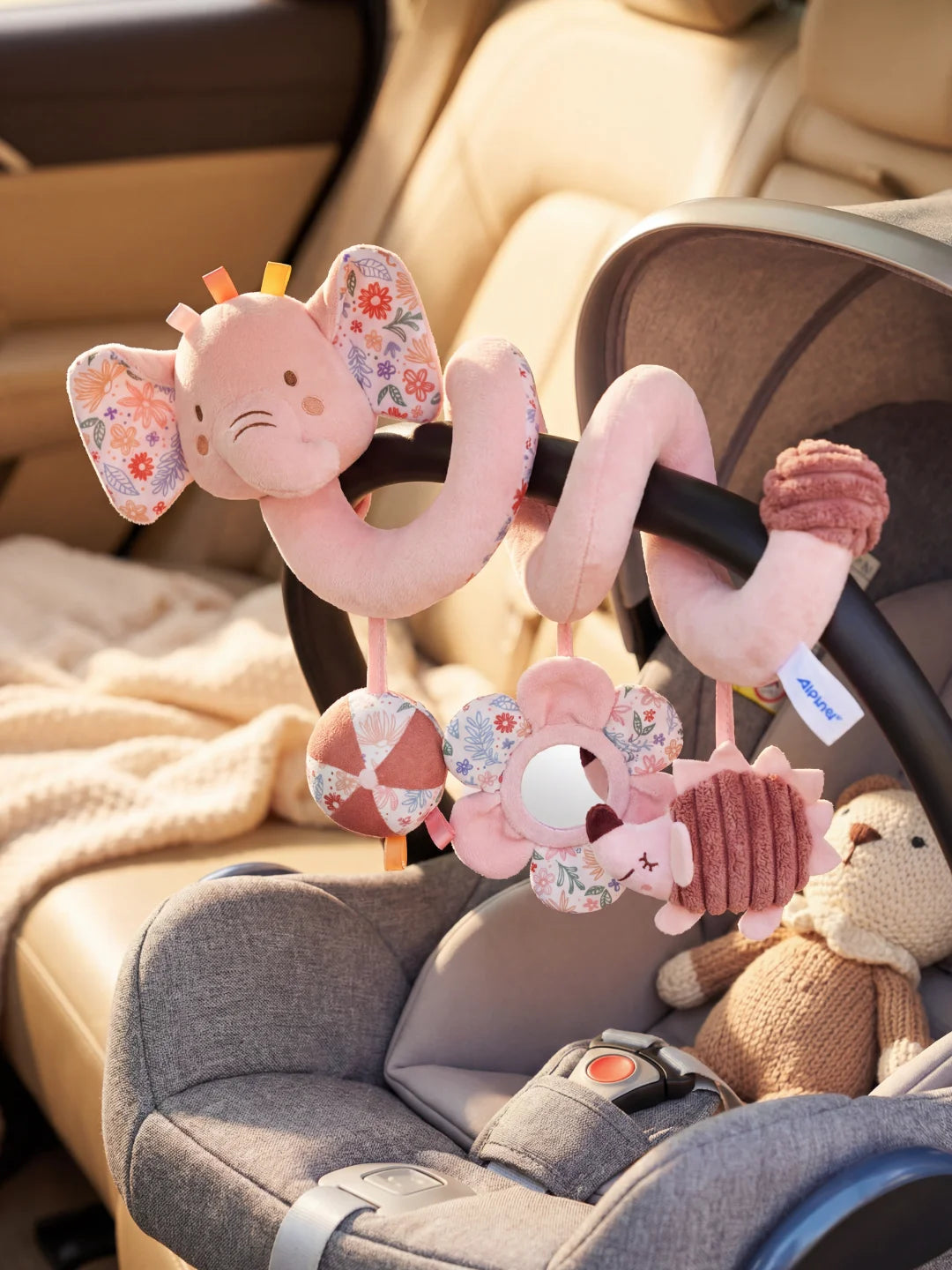Jouet de voyage éléphant rose pour bébé installé sur la poignée d'un siège auto.