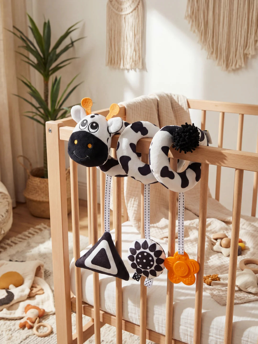 Spirale d'éveil contrastée noir et blanc avec tête de vachette fixée sur un lit de bébé.