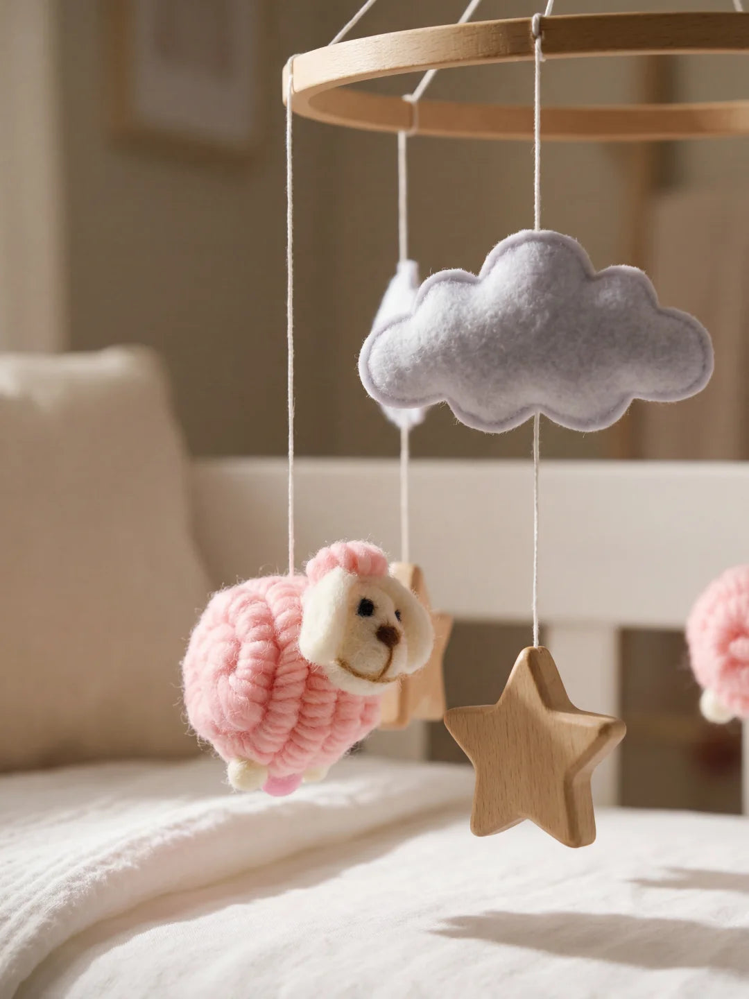 Détail d'une figurine de mouton rose et d'un nuage en feutrine grise suspendus à un mobile de lit.