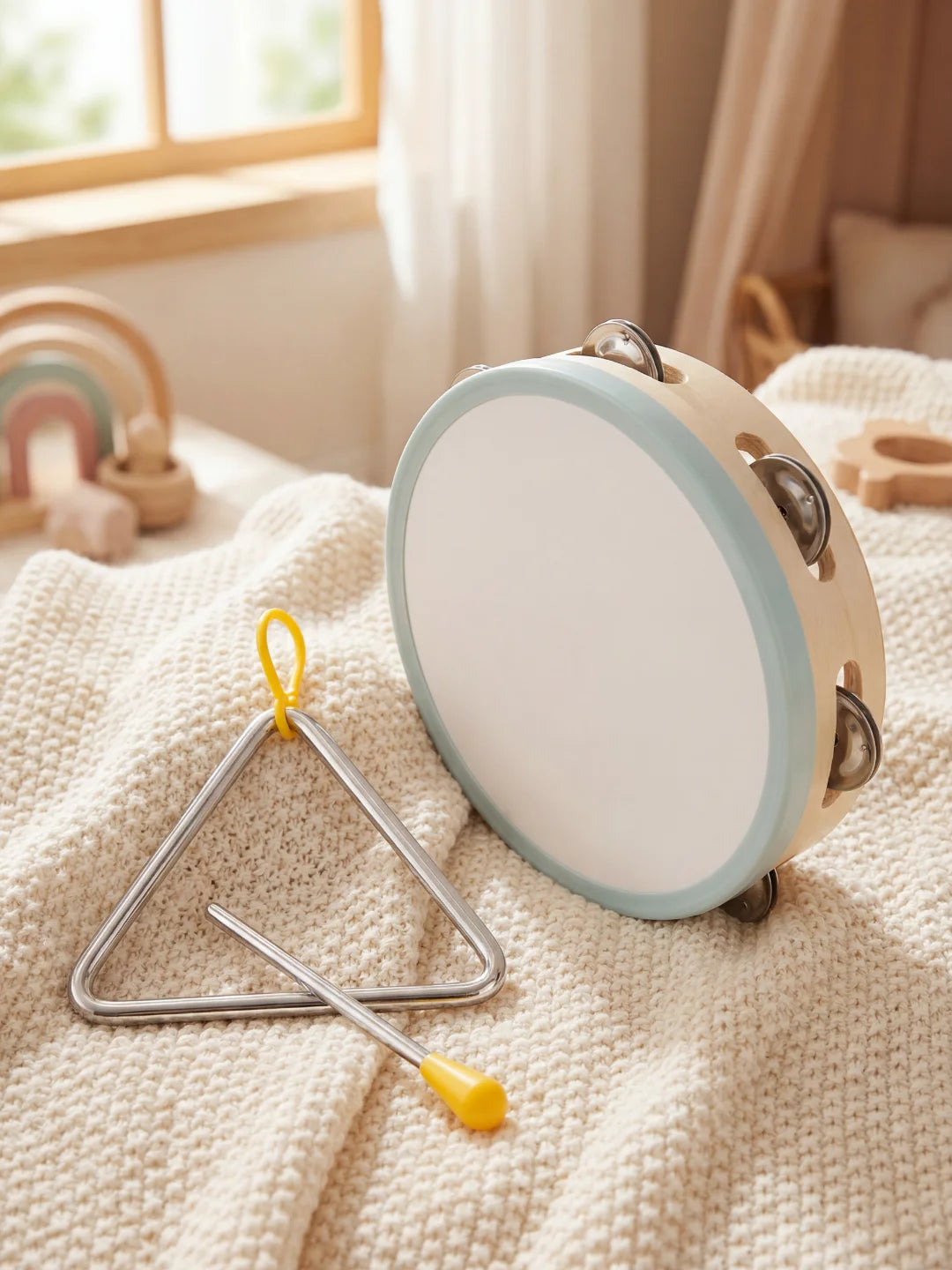 Tambourin en bois et triangle musical posés sur un tissu doux.
