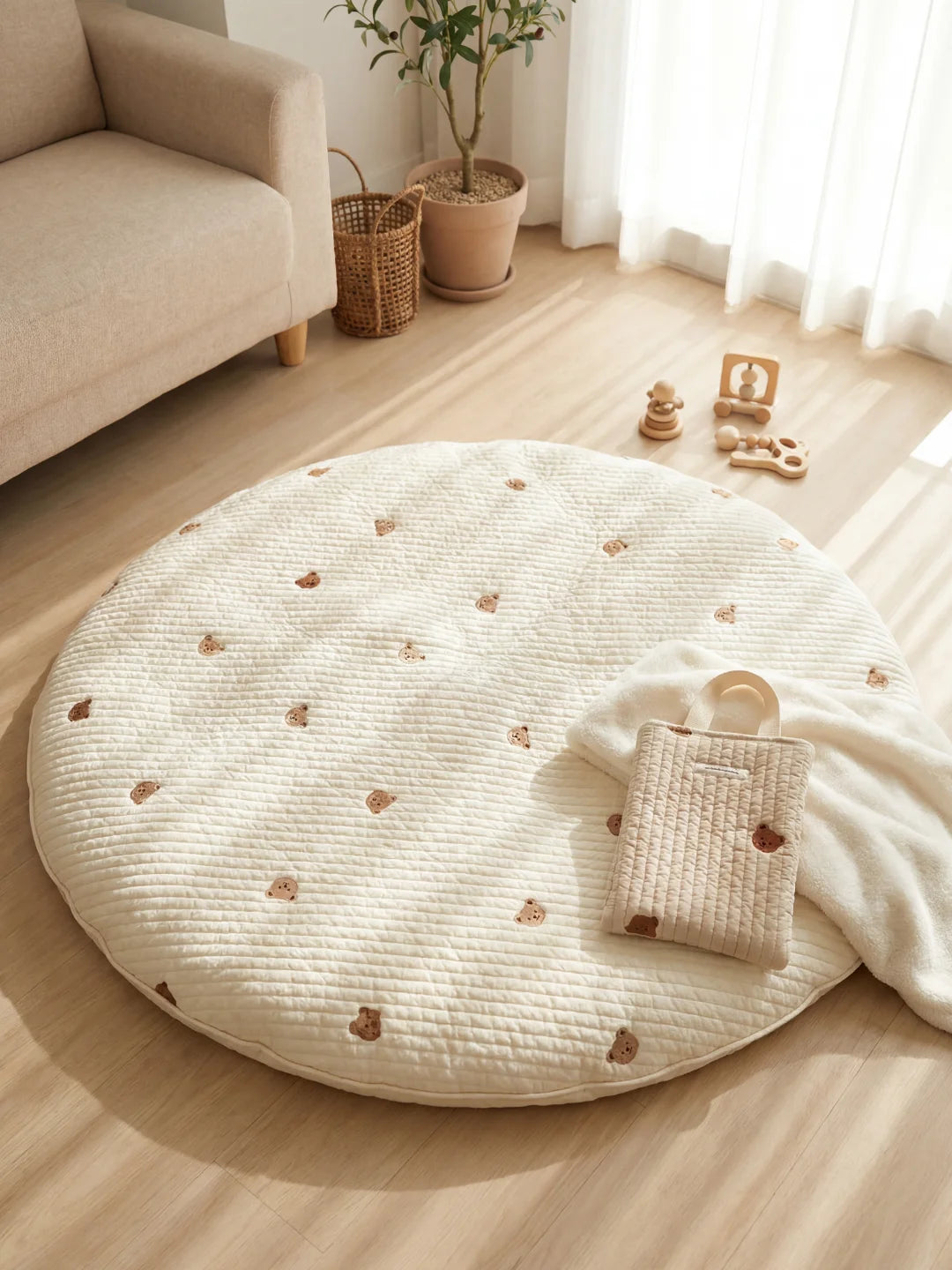 Tapis d'éveil rond beige avec petites broderies d'oursons posé dans un salon lumineux à côté d'un sac assorti.