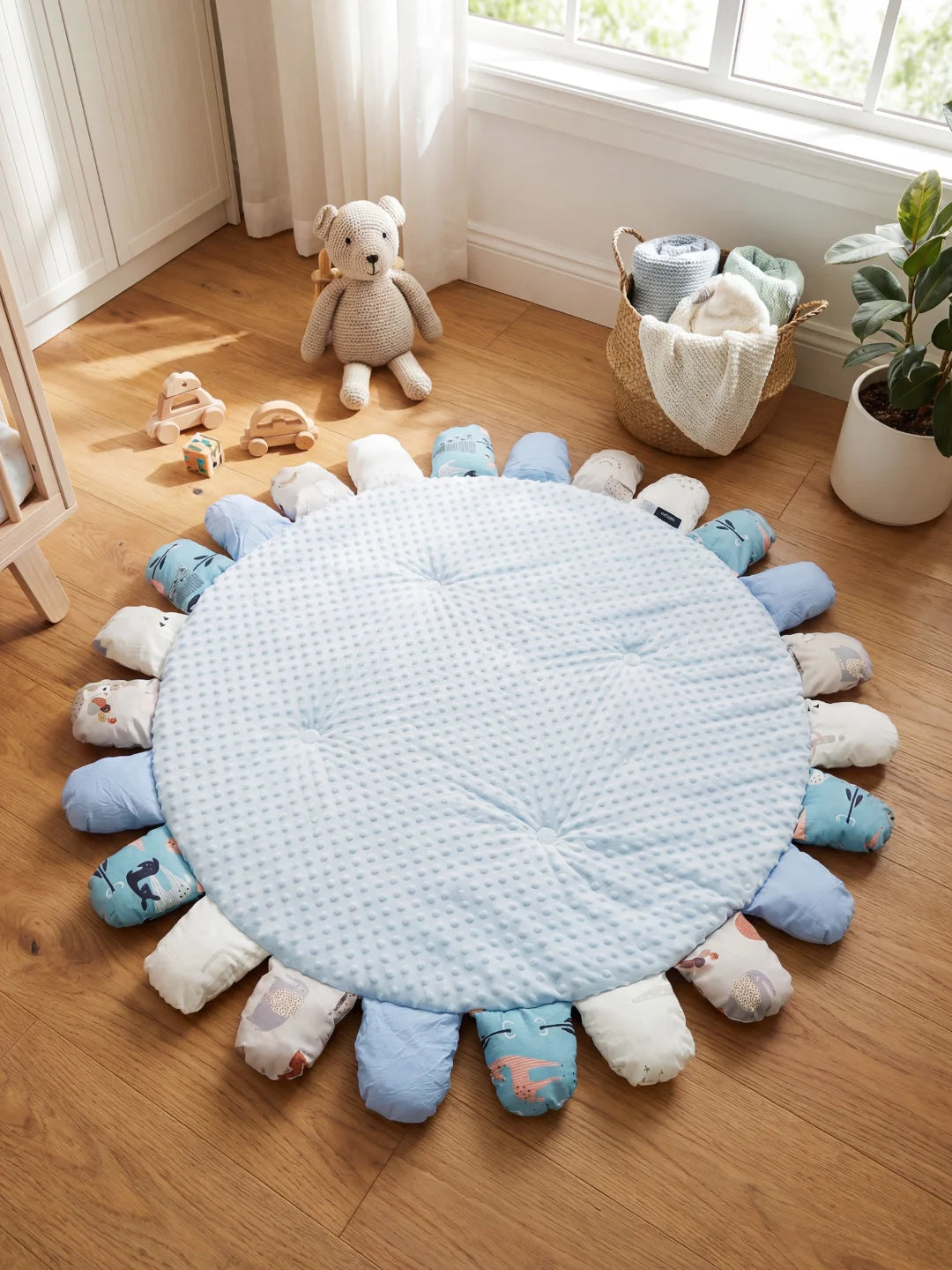 Tapis d'éveil rond bleu ciel en tissu minky avec pétales rembourrés illustrés de baleines et d'animaux dans une chambre lumineuse.