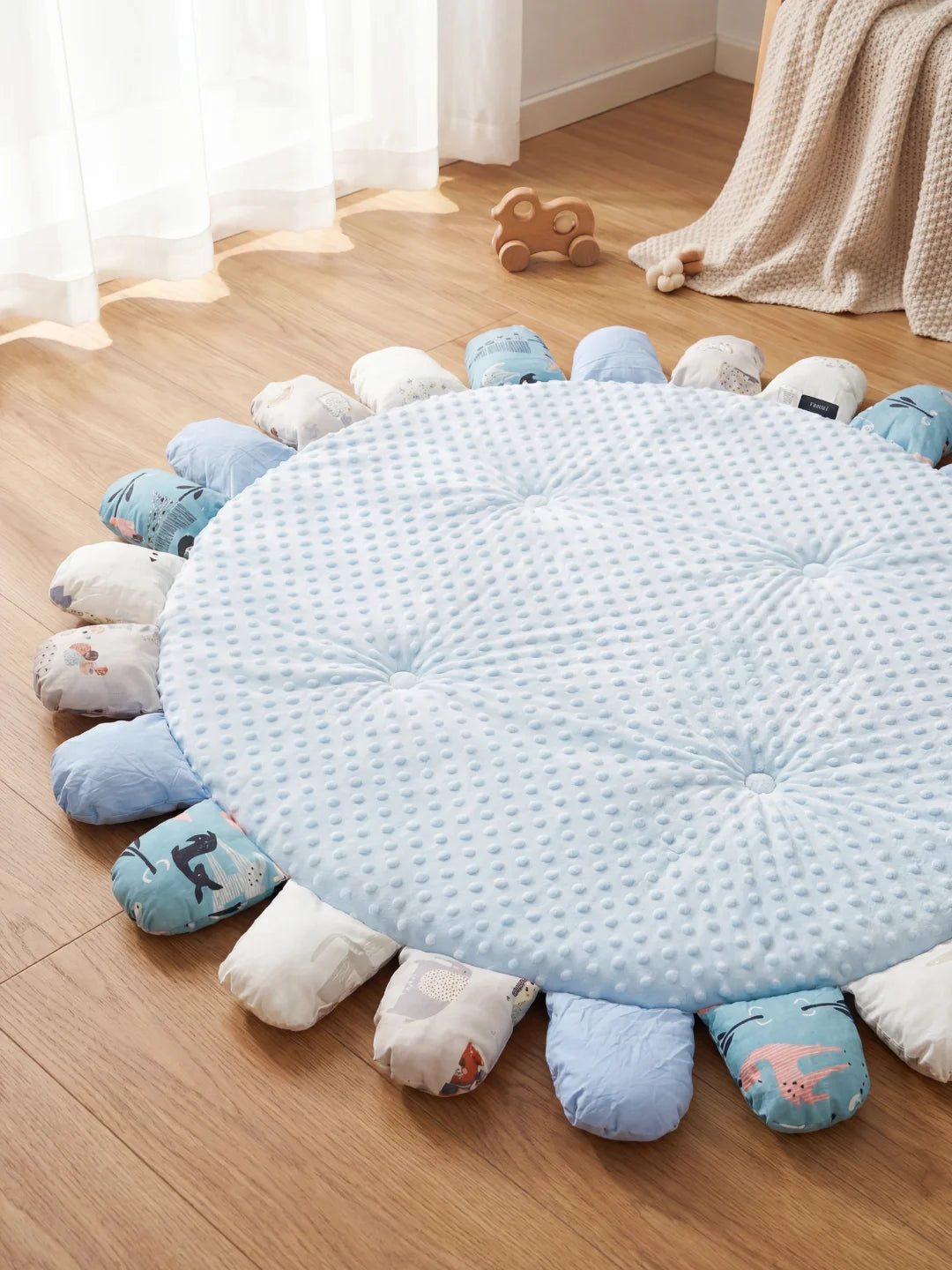 Vue d'ensemble d'un tapis de sol bleu pour bébé avec texture sensorielle à picots et pétales aux motifs marins posé sur un parquet.