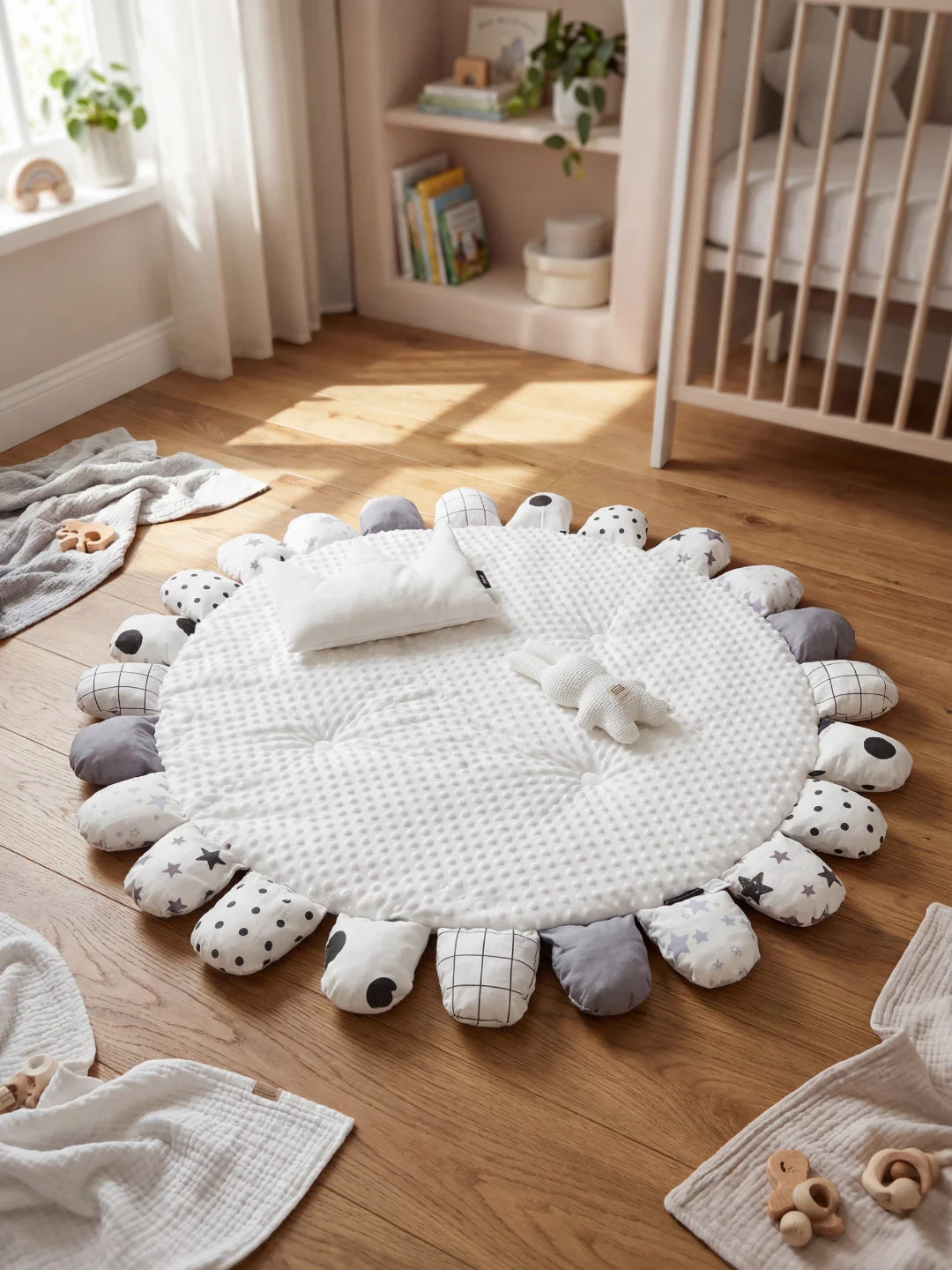 Tapis de sol pour bébé blanc à texture sensorielle minky, entouré de pétales rembourrés gris et noirs sur un parquet clair.