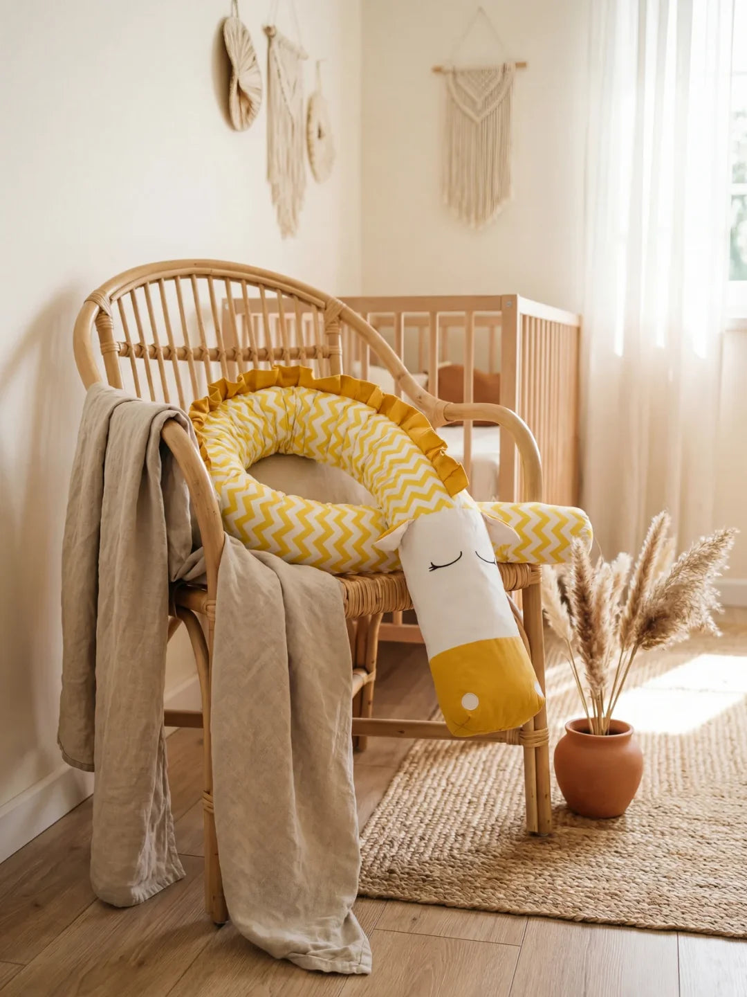 Tour de lit traversin bébé chevron jaune posé sur fauteuil en rotin chambre bébé