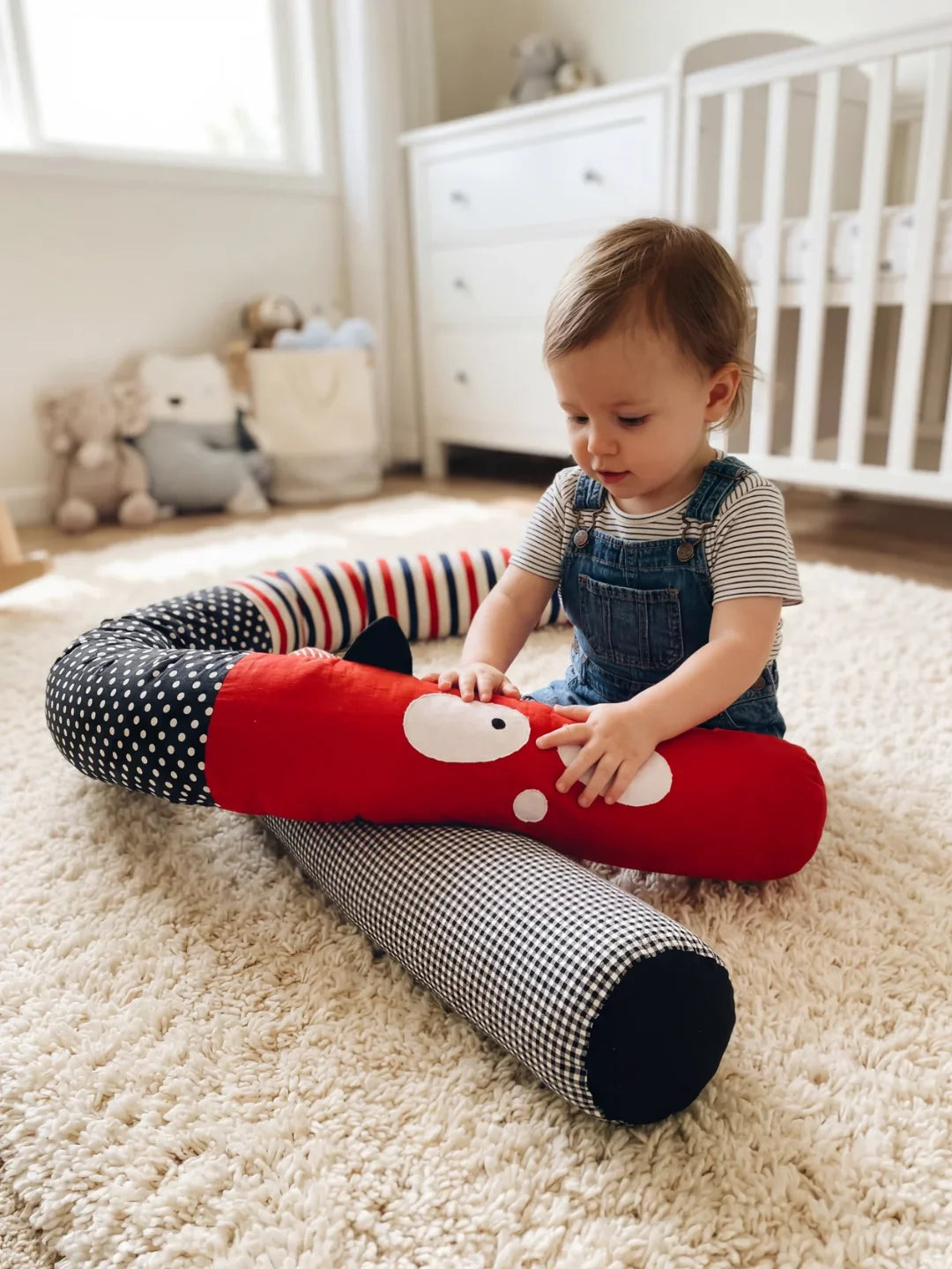 Bébé jouant avec un tour de lit traversin monstre rouge dans une chambre