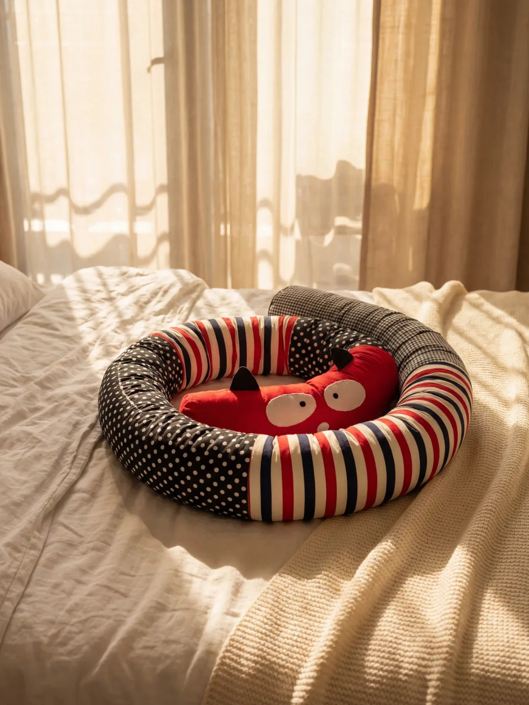 Tour de lit traversin bébé monstre rouge enroulé sur un lit avec lumière naturelle