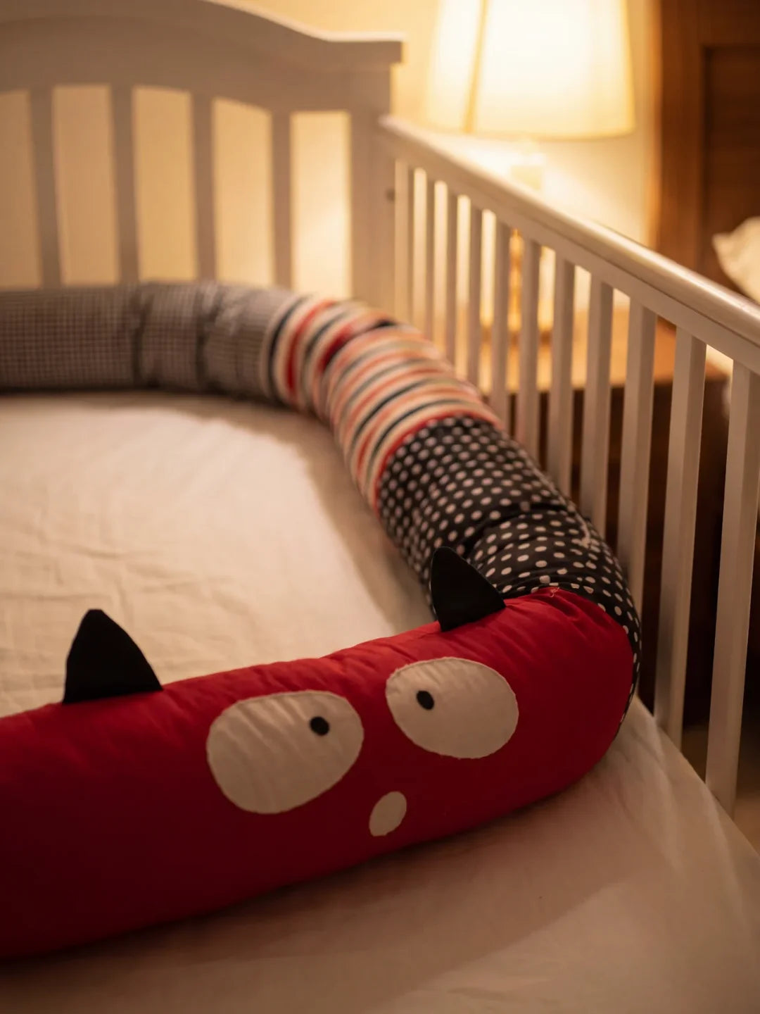 Tour de lit traversin bébé monstre rouge installé dans un lit à barreaux blanc