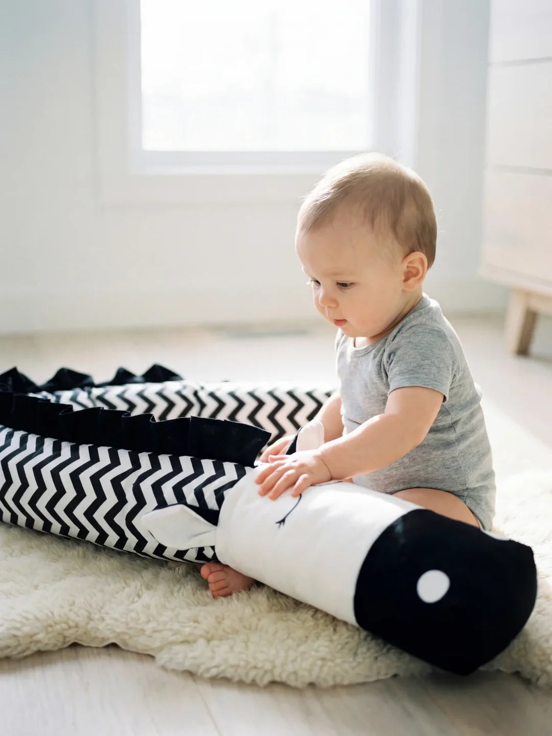 Bébé assis jouant avec tour de lit traversin chevron noir et blanc