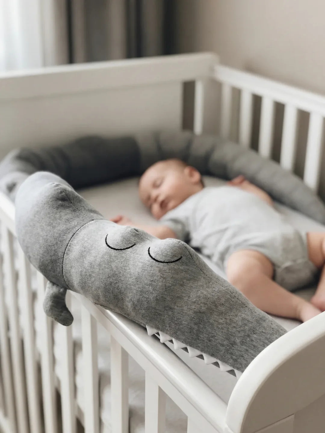 Bébé endormi dans son lit protégé par un tour de lit traversin crocodile gris