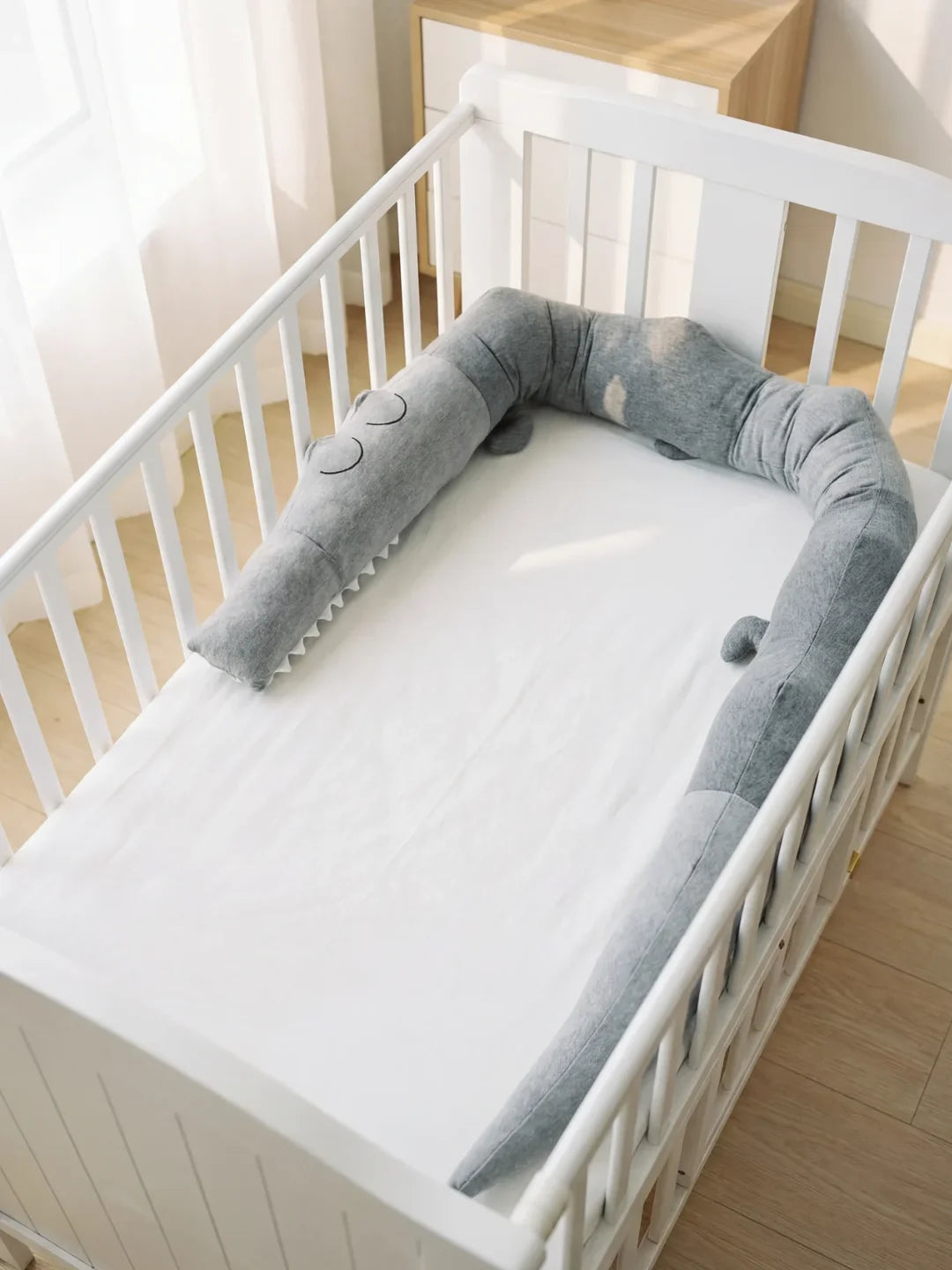 Tour de lit traversin crocodile gris installé dans un lit à barreaux blanc