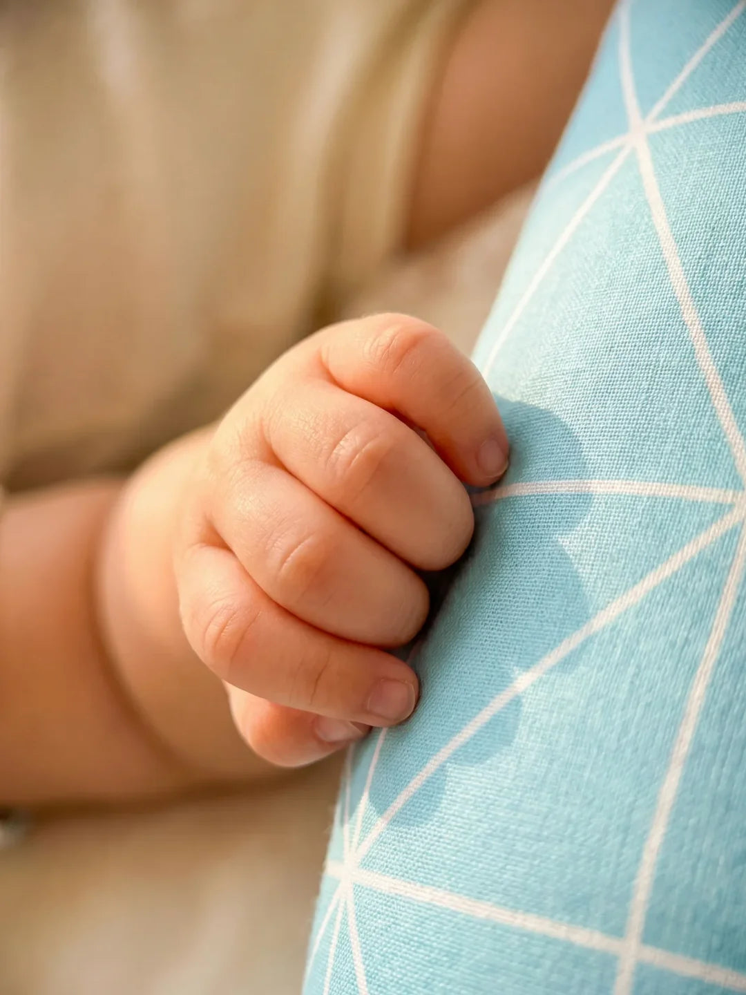 Détail main de bébé tenant le tour de lit traversin géométrique bleu