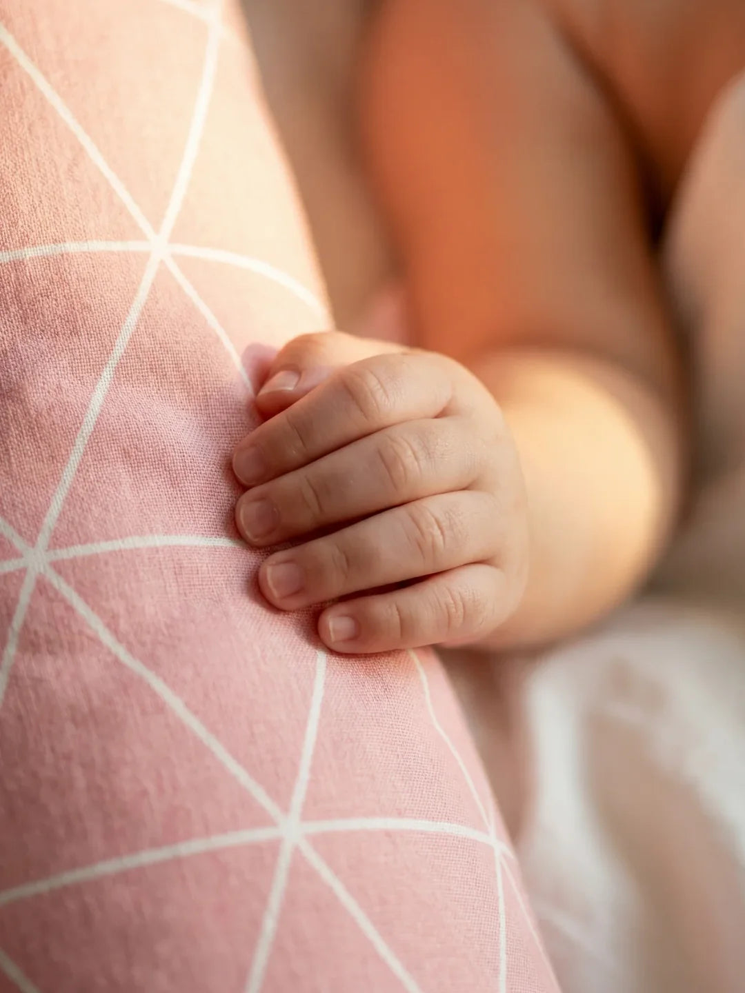 Détail main de bébé agrippant le tour de lit traversin géométrique rose