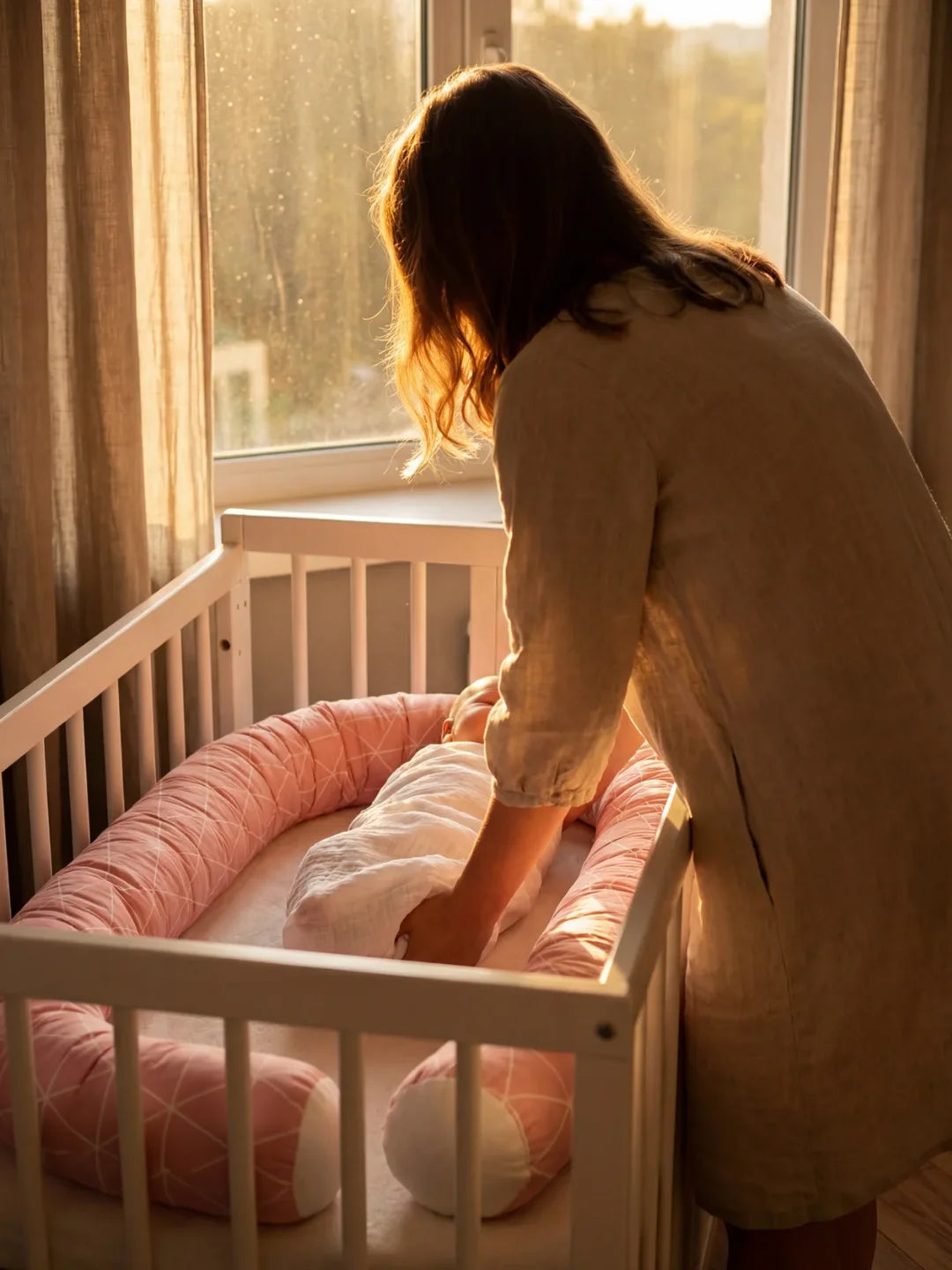 Maman installant bébé dans lit avec tour de lit traversin géométrique rose