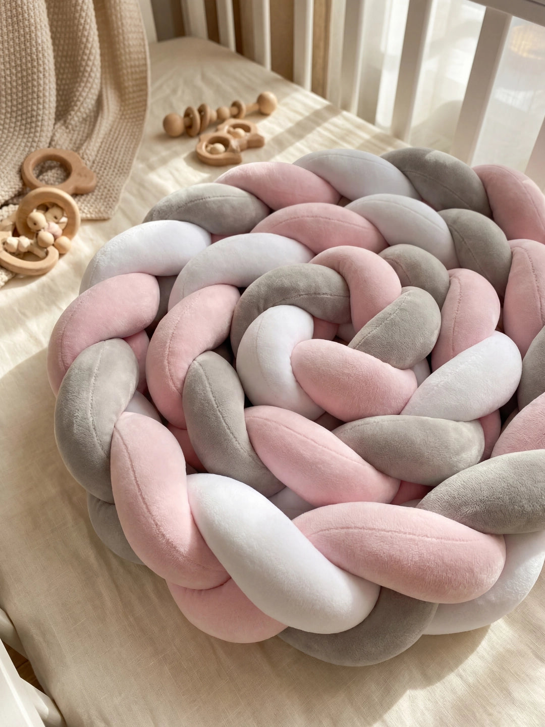 Tour de lit tressé enroulé en forme de coussin rond sur un matelas, accompagné de jouets de dentition en bois.