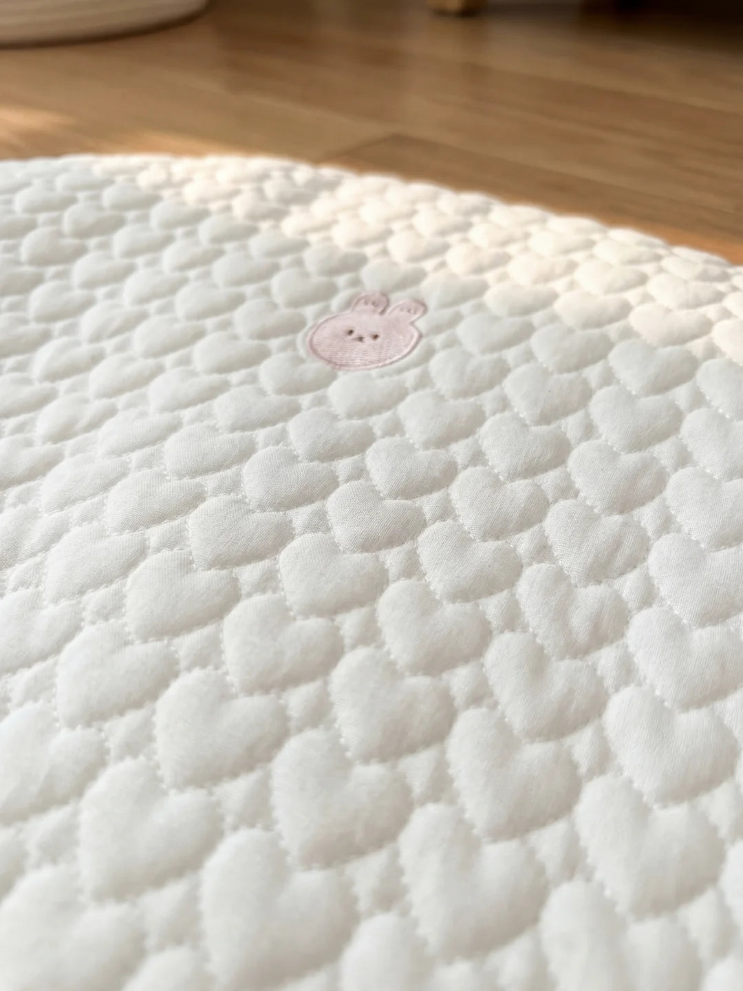 Détail de la broderie lapin rose sur la texture matelassée en cœurs d'un tapis d'éveil pour bébé.