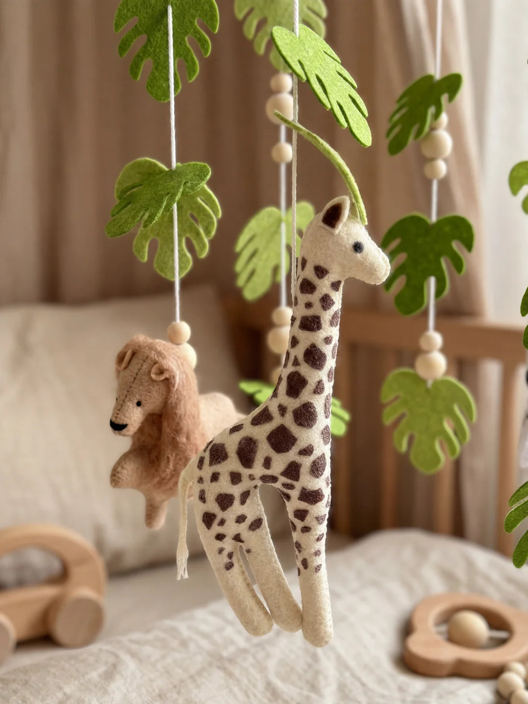 Gros plan sur la girafe en tissu et les détails des feuilles de monstera d'un mobile bébé.