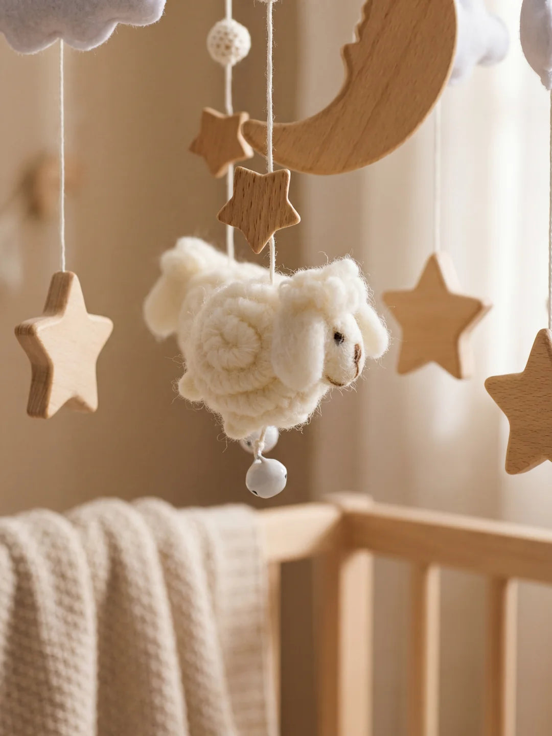 Gros plan sur un petit mouton blanc et une étoile en bois massif suspendus au berceau.