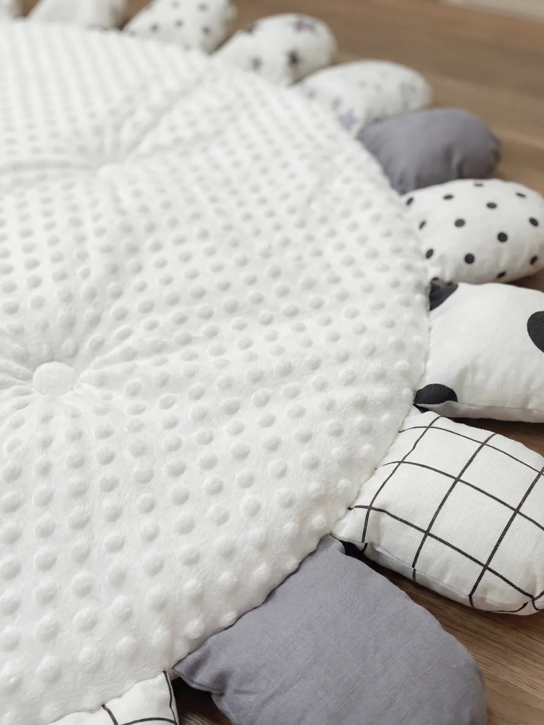 Gros plan sur la texture minky à picots d'un tapis de sol pour bébé et les détails des pétales aux motifs étoiles et pois.