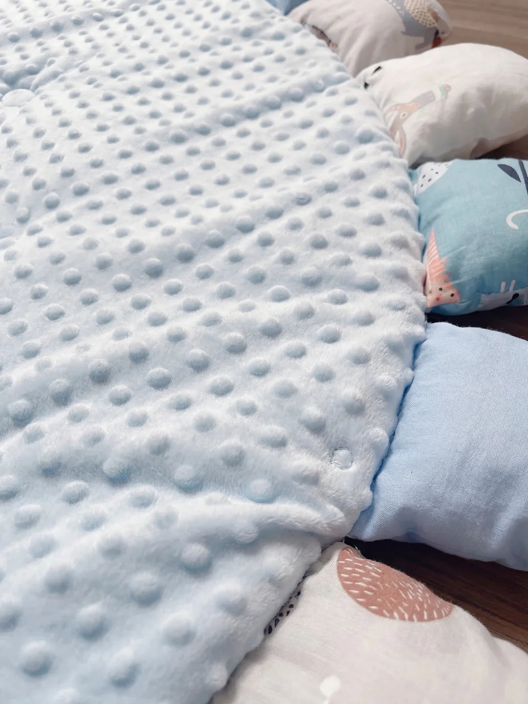 Gros plan sur le tissu minky bleu ciel et le détail d'un pétale avec un motif de baleine sur un tapis d'éveil sensoriel.