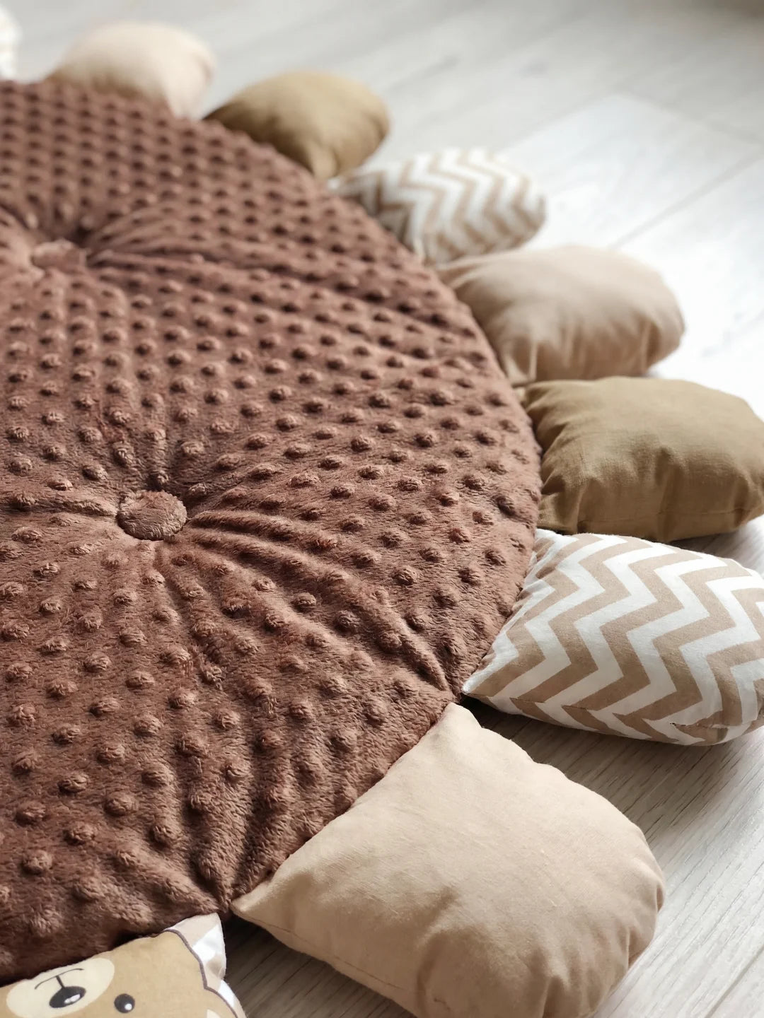Gros plan sur la texture douce à picots du tapis d'éveil marron et les détails des pétales aux motifs chevrons et ours.