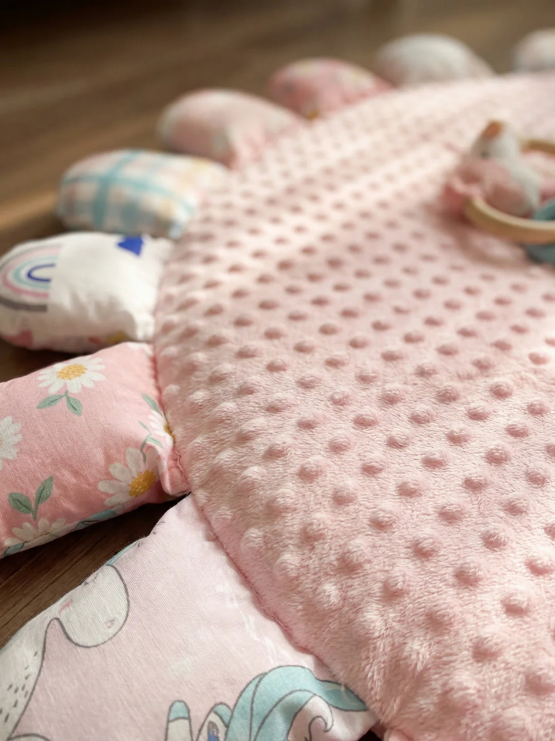 Gros plan sur la texture douce à picots (minky) du tapis d'éveil rose et les détails des pétales aux motifs variés.
